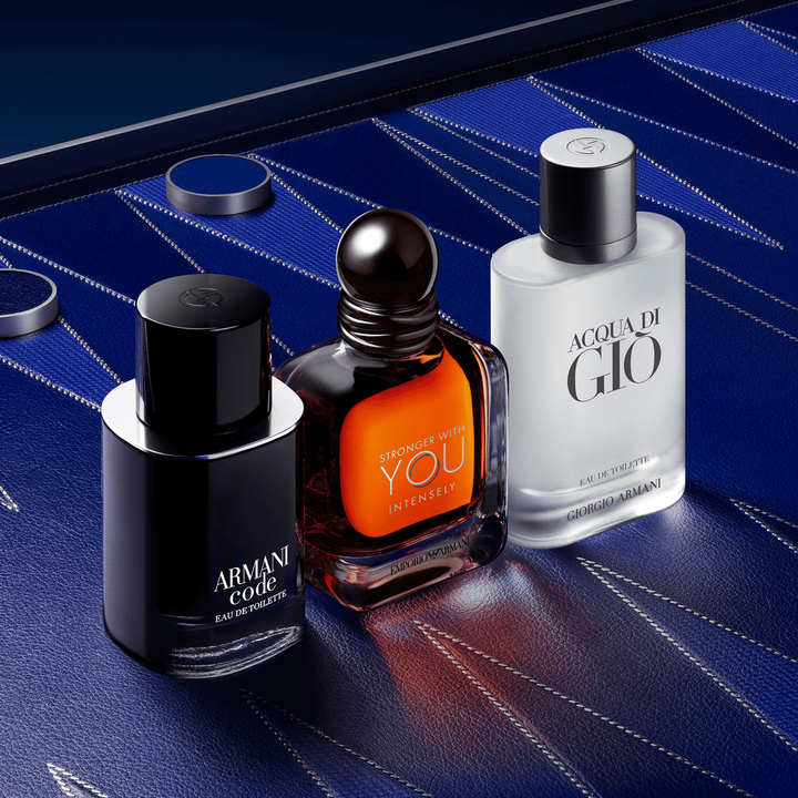 A sophisticated trio of Armani men's icons: Armani Code, Stronger With You Powerfully, and Acqua di Gio. The bottles stand on a luxurious deep blue leather-textured background with couture geometric patterns, embodying masculine elegance.