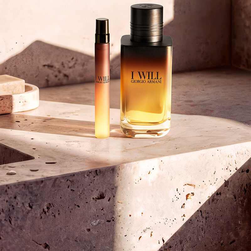 A large and a small bottle of Giorgio Armani 'I Will' fragrance on a stone surface under warm sunlight.