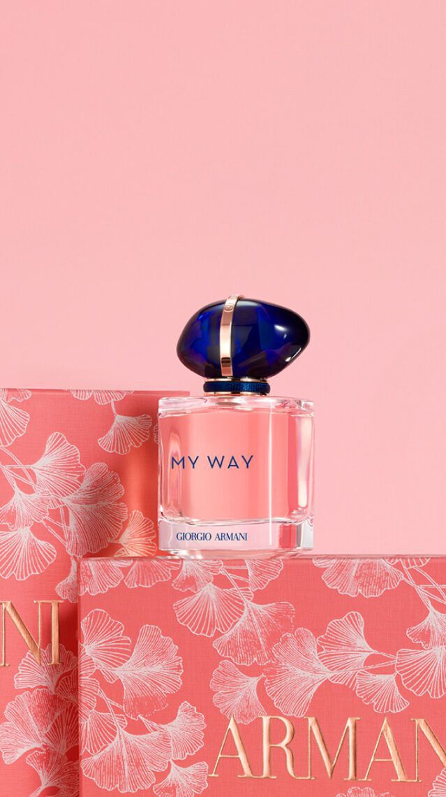 A bottle of Armani's "My Way" perfume is displayed next to its pink floral packaging against a soft pink background.