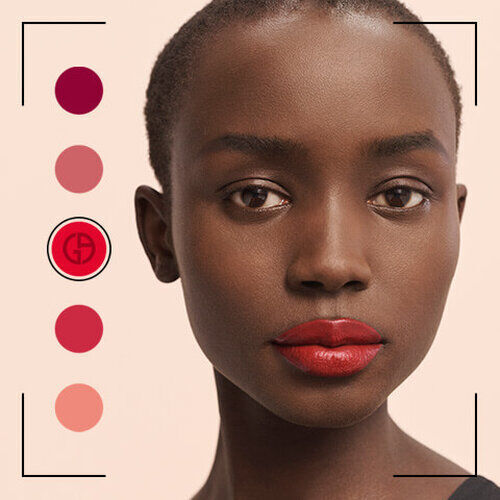 A close-up portrait of a model with short hair and deep red lips, showcasing various lip color swatches on the side. The background is a soft, neutral tone, highlighting her features.