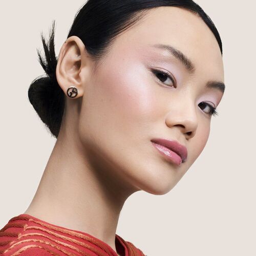 A woman with a sleek hairstyle and subtle makeup showcases elegant earrings against a neutral background.