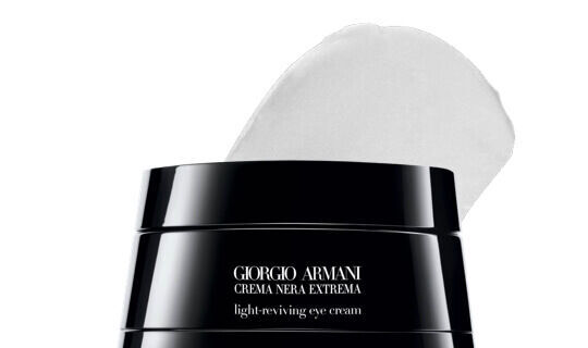 A close-up of a jar of Giorgio Armani Crema Nera Extrema light-reviving eye cream, featuring a partially lifted white cream lid.