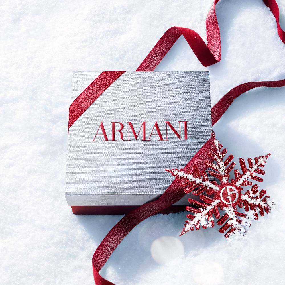 Armani beauty Holiday 2026 white gift box tied with a red ribbon and snowflake decoration on a snowy surface