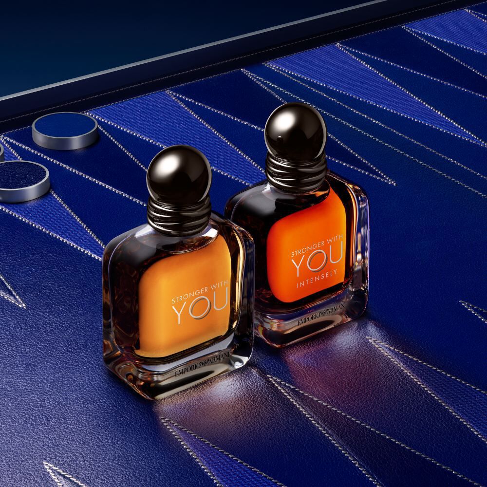 Armani STRONGER WITH YOU EAU DE TOILETTE bottles on a blue geometric background, showcasing the modern, masculine bottle design and vibrant amber hue.