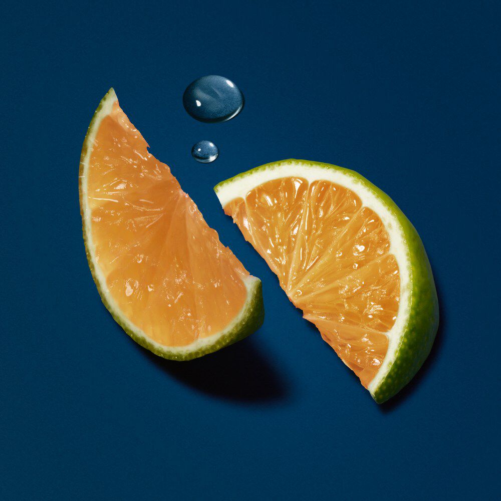 Two vibrant orange citrus fruit slices on a dark blue background, with a small droplet of water nearby.