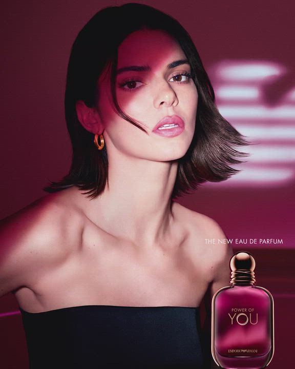 Kendall Jenner illuminated by ruby light beside the Armani Power of You perfume bottle, with the iconic eagle symbol glowing in the background.