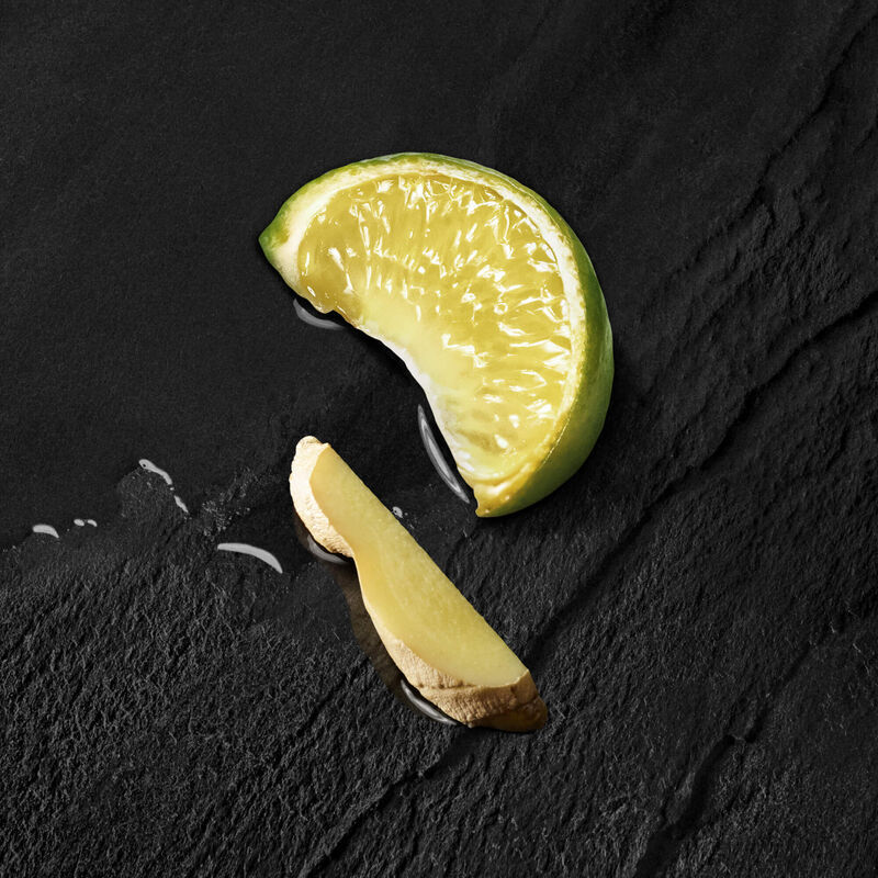 A fresh lime wedge and a slice of ginger on a dark slate surface, with a hint of juice glistening.