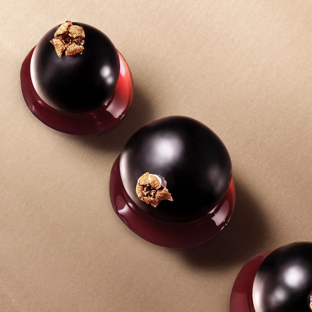 Three glossy blackcurrants with brown tops on a beige background.