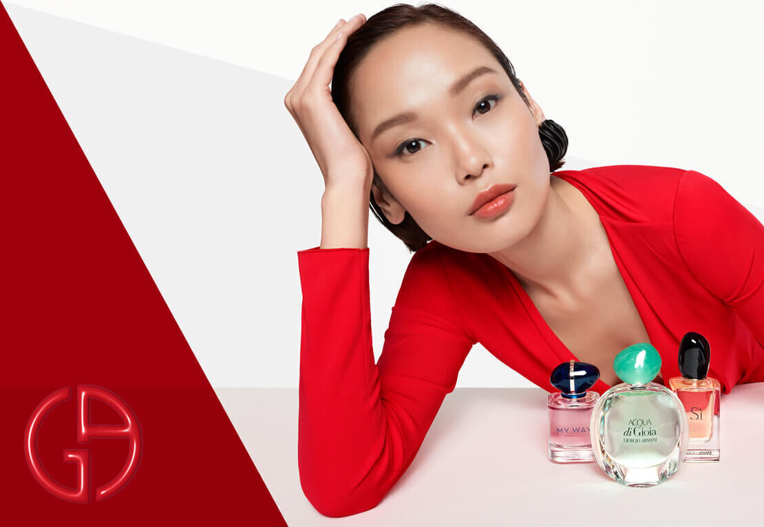 A woman in a red outfit rests her head on her hand with a neutral expression, surrounded by four perfume bottles on a white background.