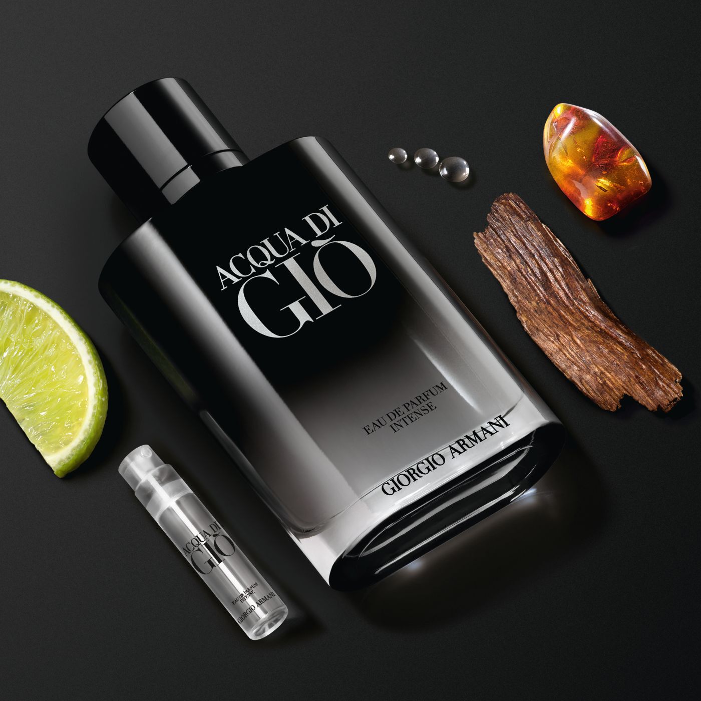 Acqua di Gio Eau de Parfum Intense bottle with lime, wood, amber, and a sample vial on a black background.