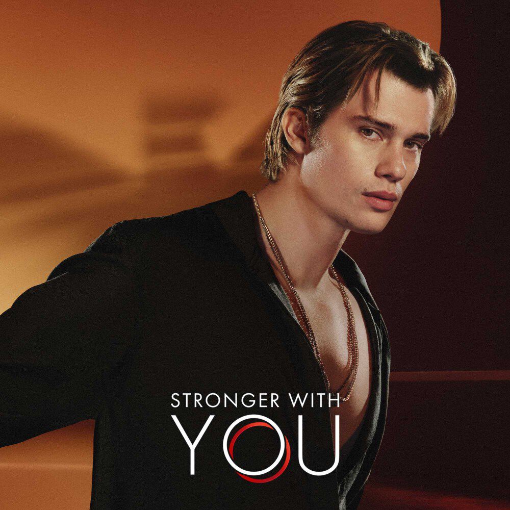 Nicholas Galitzine and the Stronger with You logo, with the blurred Emporio Armani logo behind him.
