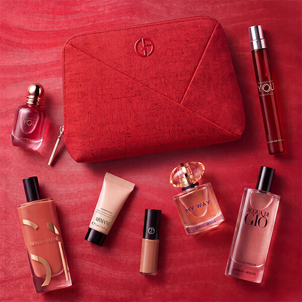 Three Armani beauty products — a lip product, Power of You fragrance and Luminous Silk foundation — displayed against a textured red backdrop.