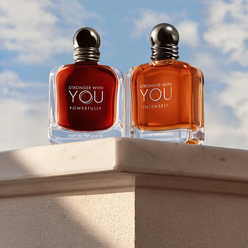 Stronger With You Powerfully and Stronger With You Intensely fragrances by Emporio Armani displayed on a stone pedestal against a blue sky.​