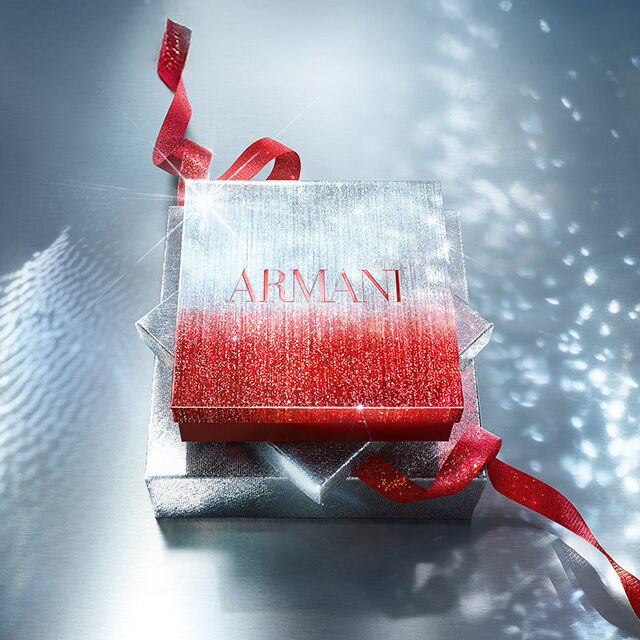 Glittery Armani gift box with red ribbon on a sparkling surface.