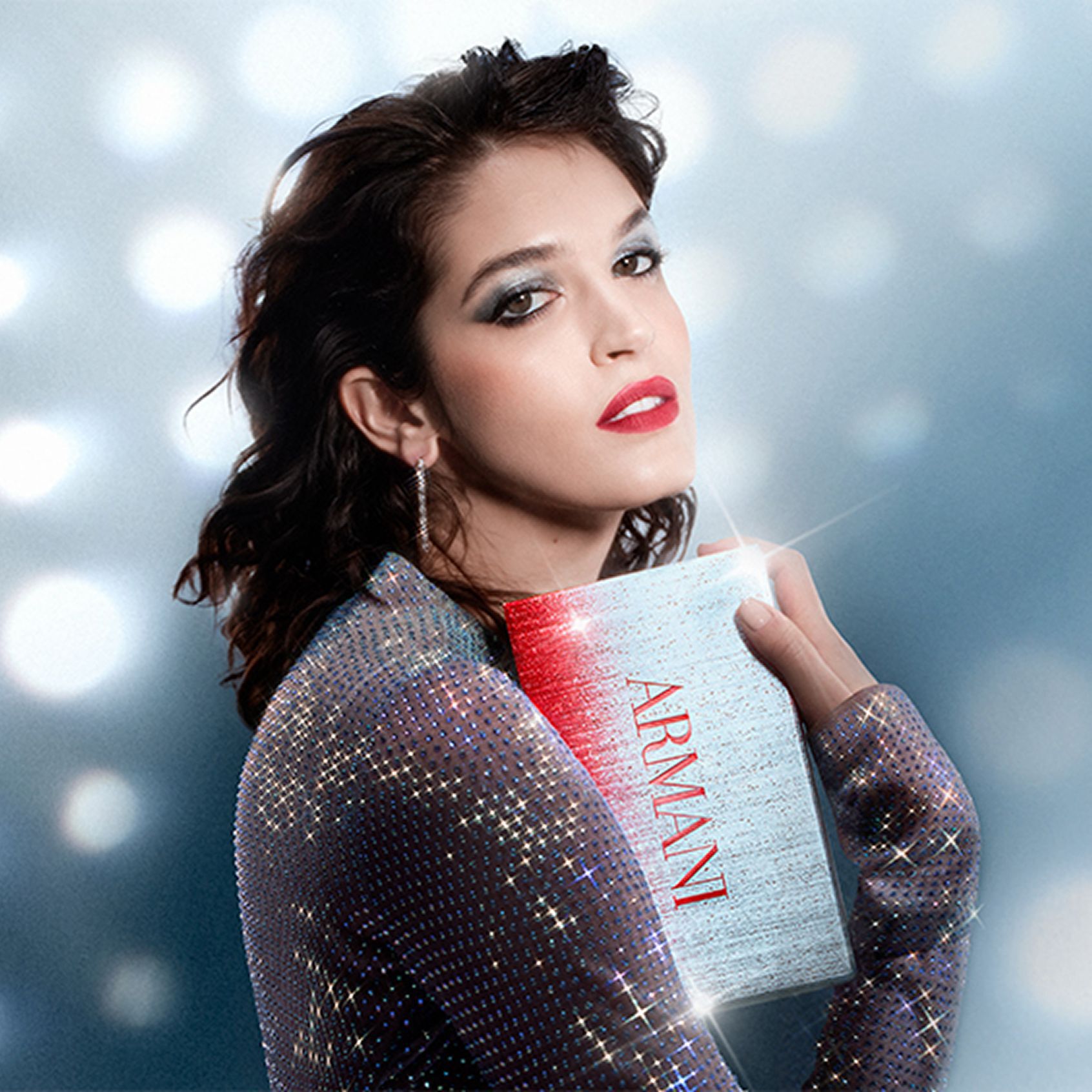 Model in a glamorous setting with dramatic lighting, wearing Armani earrings and a sparkling outfit, highlighting the brand’s holiday style.