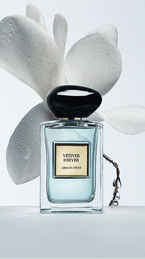 Bottle of Armani/Prive Vetiver D’Hiver against a light blue  with floral ingredients.
