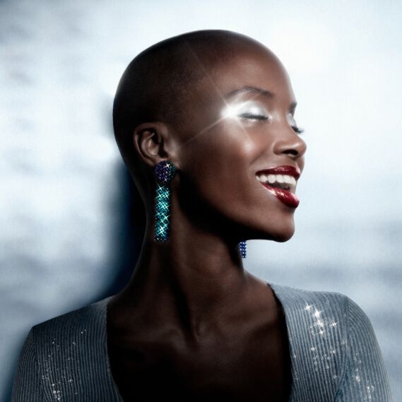 ing woman with shaved head, sparkling eye makeup, and colorful statement earrings.