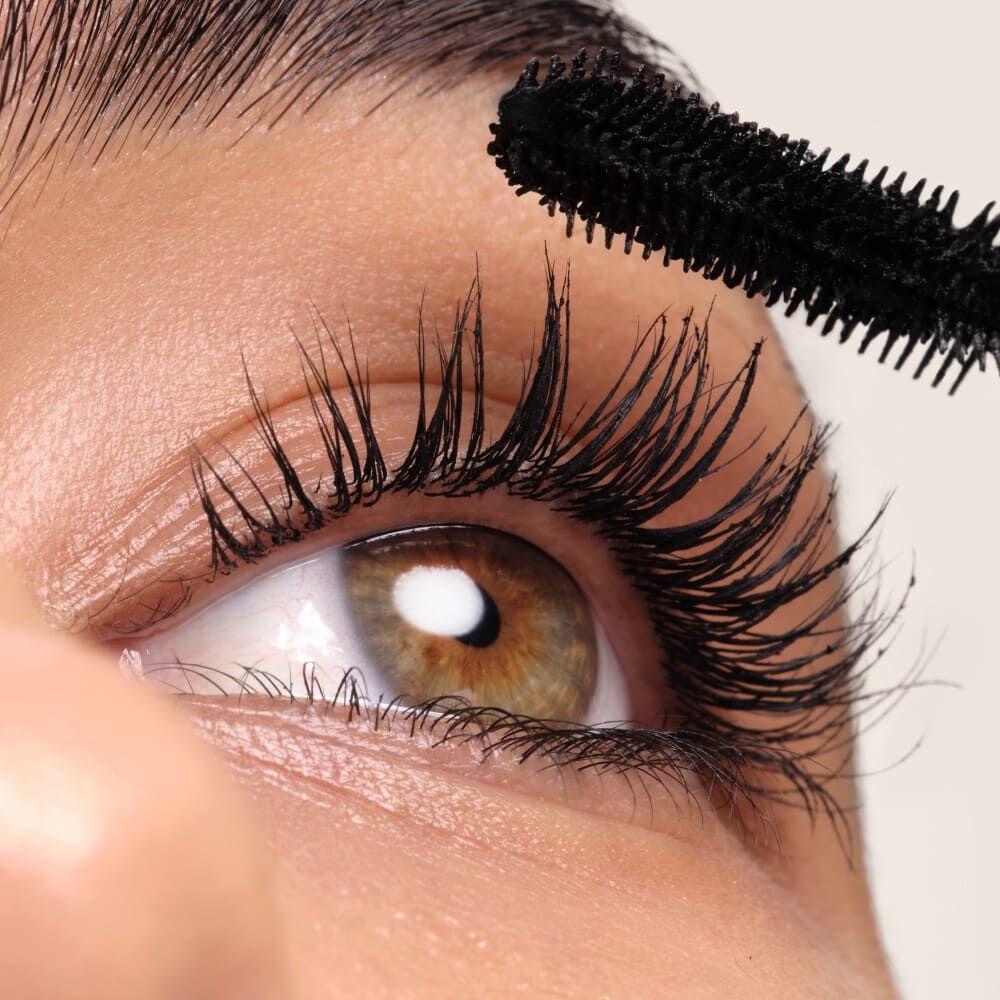 Close-up of an eye with long, voluminous lashes being coated with black mascara.