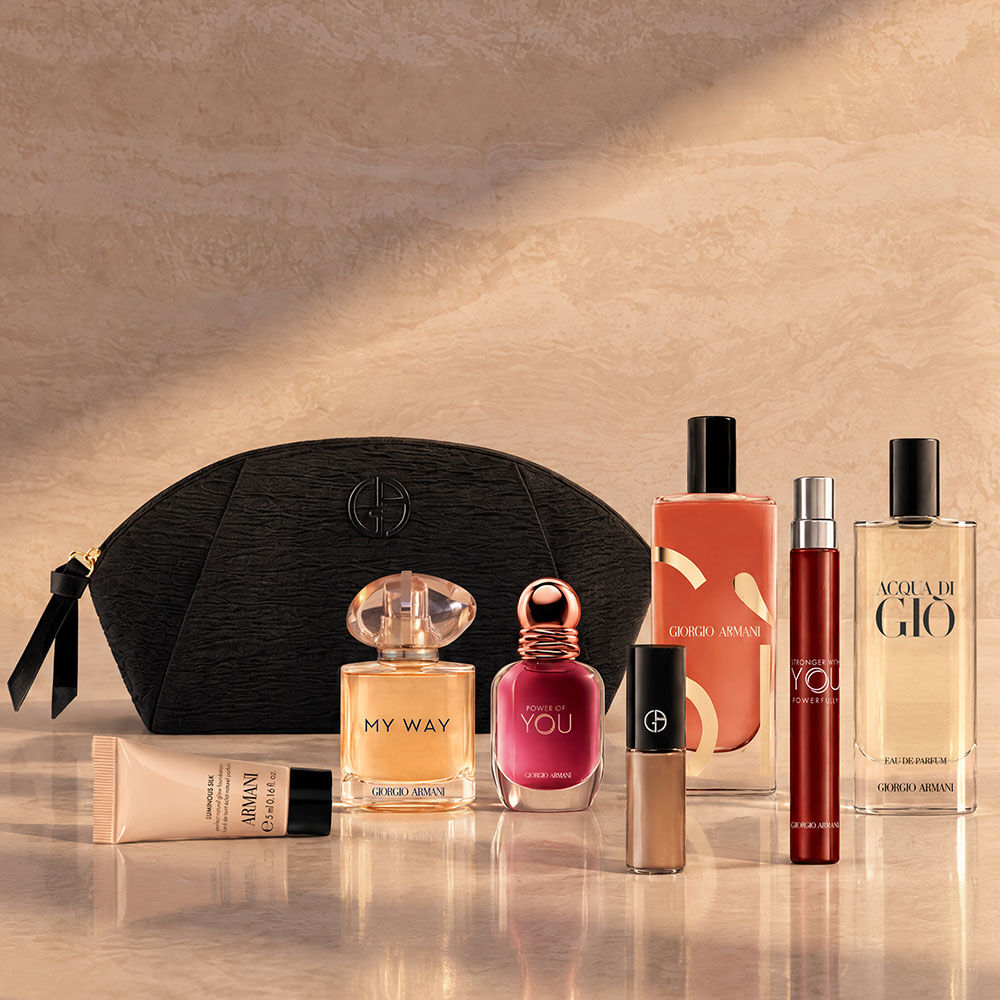 "Black Armani Beauty pouch displayed with assorted fragrances, makeup and skincare products against a beige backdrop.  "