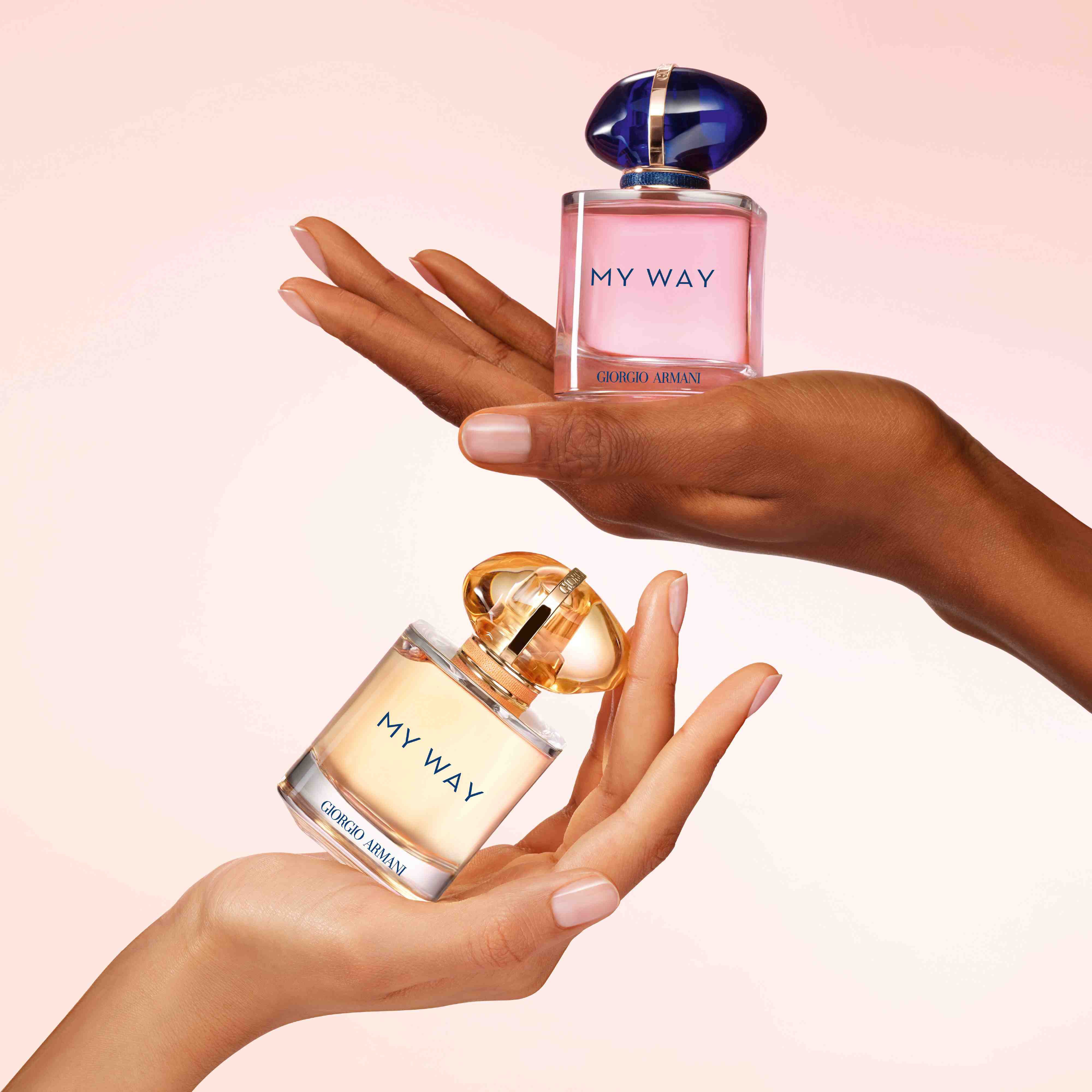 Two hands of different skin tones each holding a bottle of Giorgio Armani My Way fragrance.