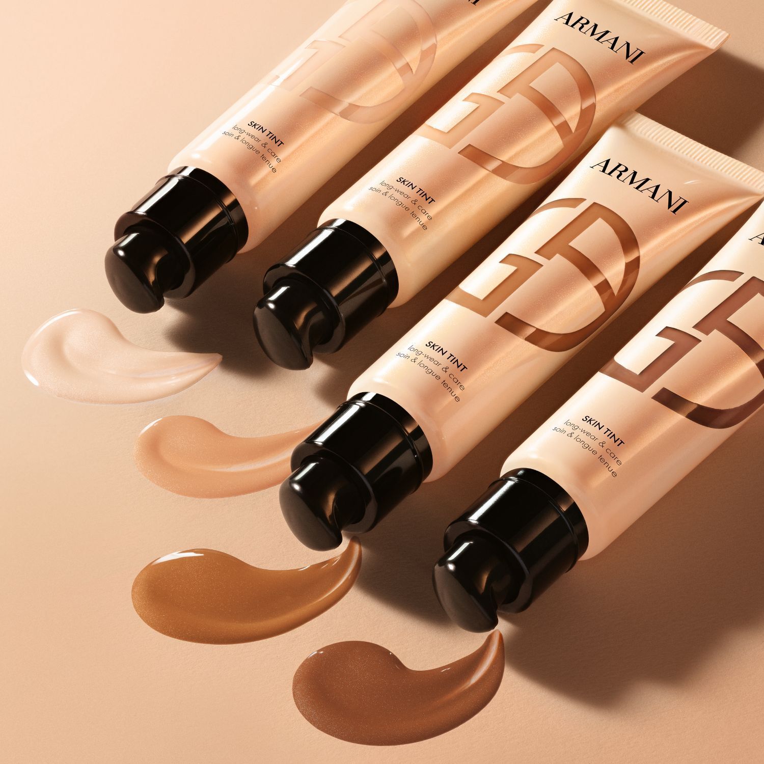 Four Armani Skin Tint tubes with dispensed swatches showing a range of shades.