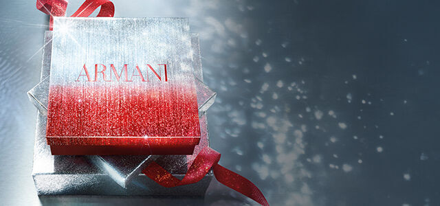 Armani gift box in sparkling red and silver with a red ribbon, set against a shimmering background.