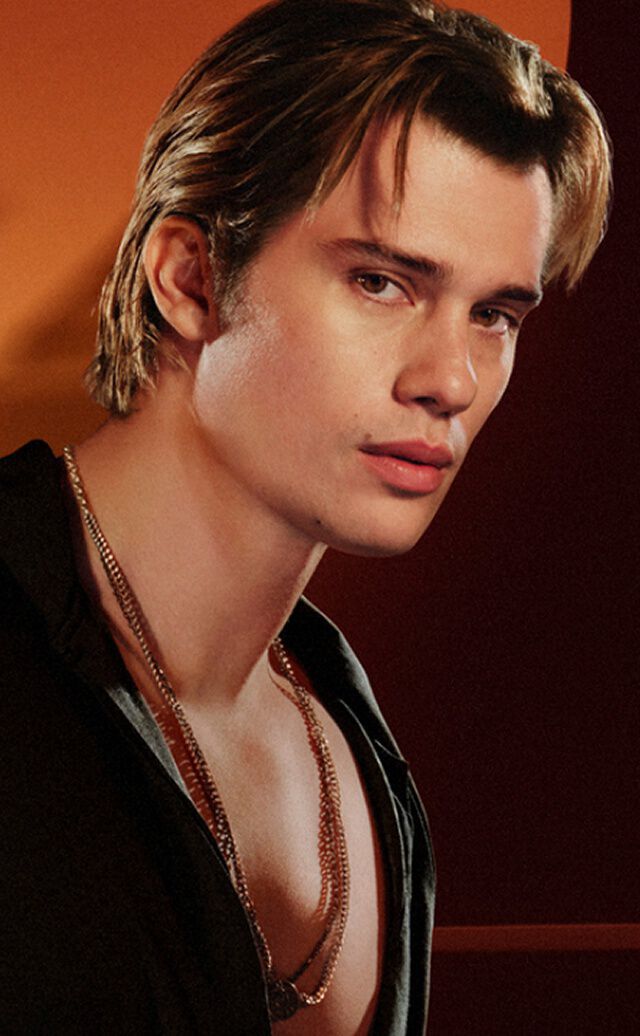 " An advertisement for the Emporio Armani ""Stronger With You"" fragrance range. On the left, a young man with light brown hair wears a black shirt and silver necklaces, looking towards the camera with a serious gaze. On the right, a product carousel under the title ""EVERY FACET OF STRONGER WITH YOU"" displays three different fragrance bottles. The central highlighted bottle is ""Stronger With You Powerfully"" in a 50ml size, priced at £74.00, with an ""ADD TO CART"" button below it. Navigation arrows and a slider bar are also visible. "