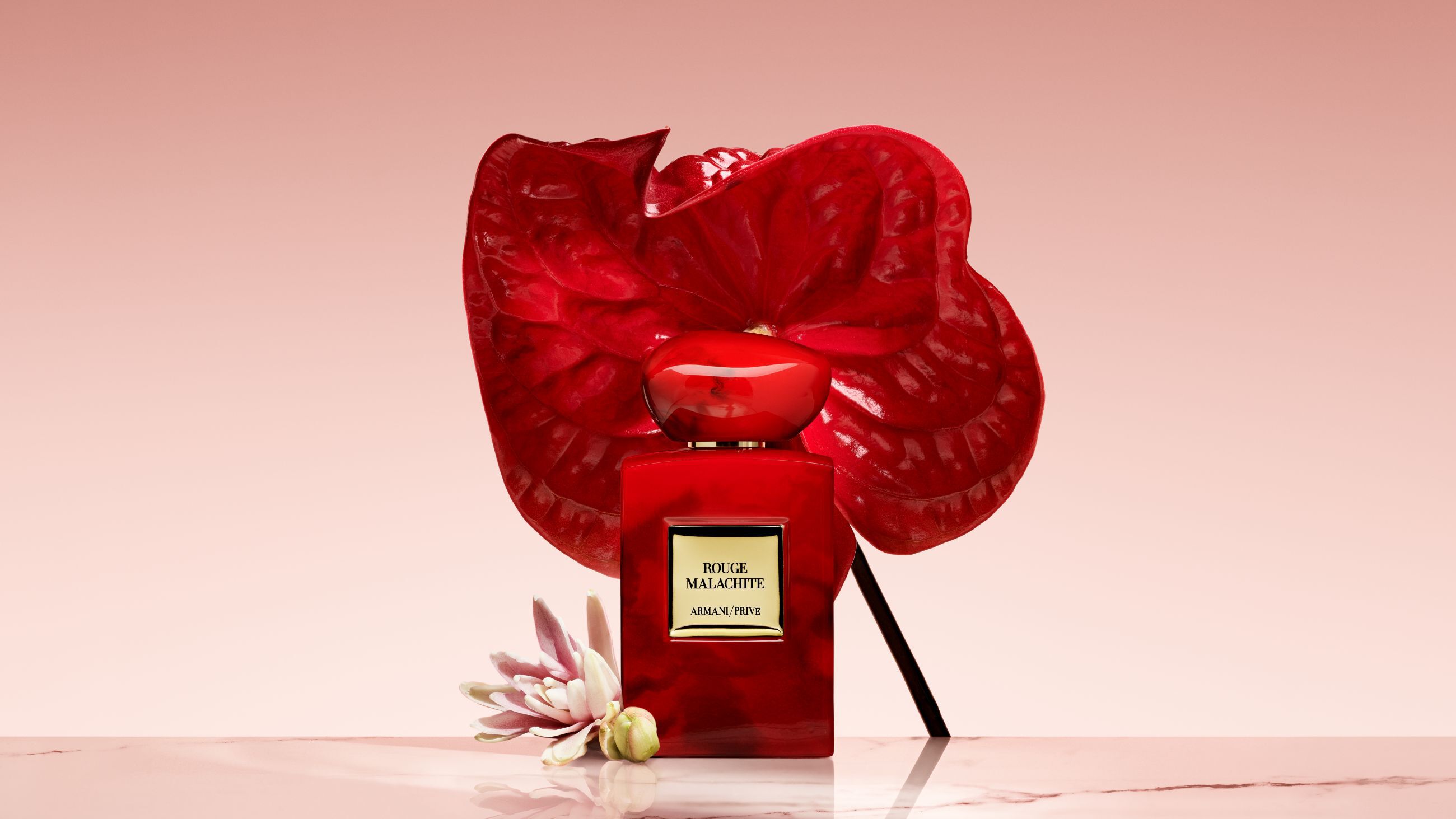 Armani/Prive Rouge Malachite perfume bottle in front of a large, vibrant red flower.