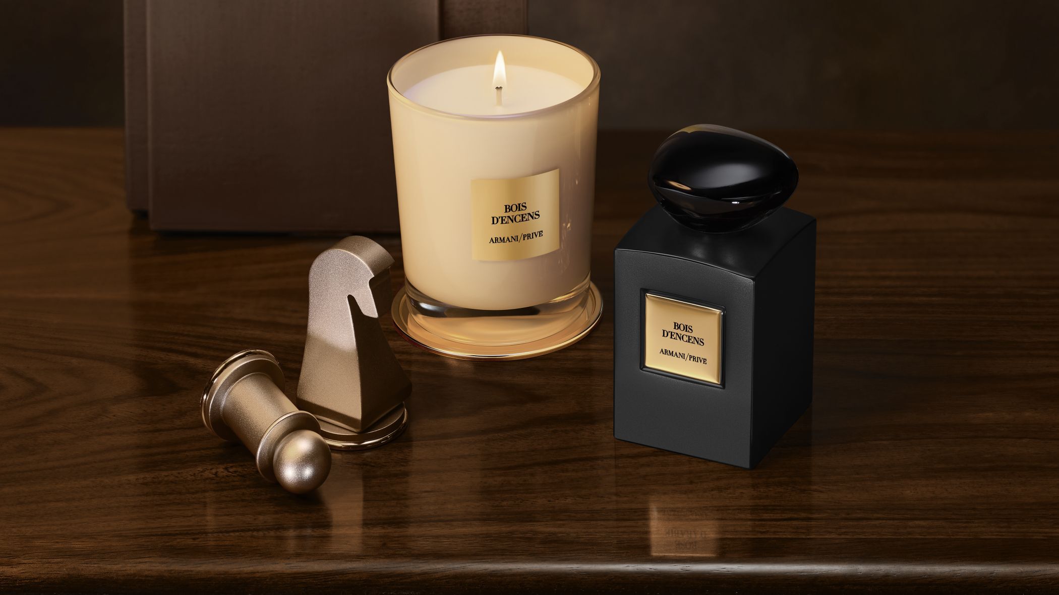 Armani/Prive Bois d'Encens perfume bottle and lit candle next to chess pieces on a wooden table.