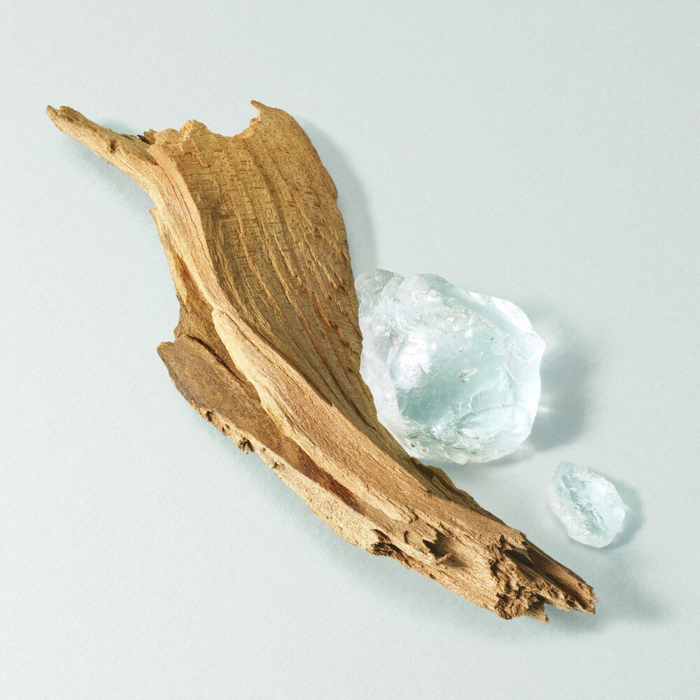 A piece of driftwood beside two translucent, icy-blue stones on a light backdrop.