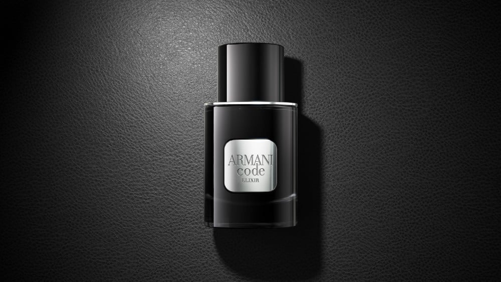 A black bottle of Armani Code Elixir perfume rests elegantly on a matching black surface, creating a sophisticated monochrome look