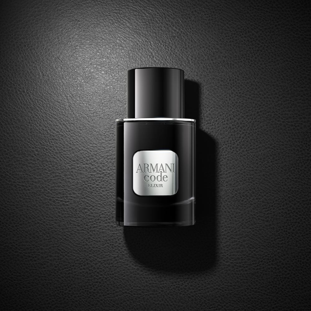A black bottle of Armani Code Elixir perfume rests elegantly on a matching black surface, creating a sophisticated monochrome look